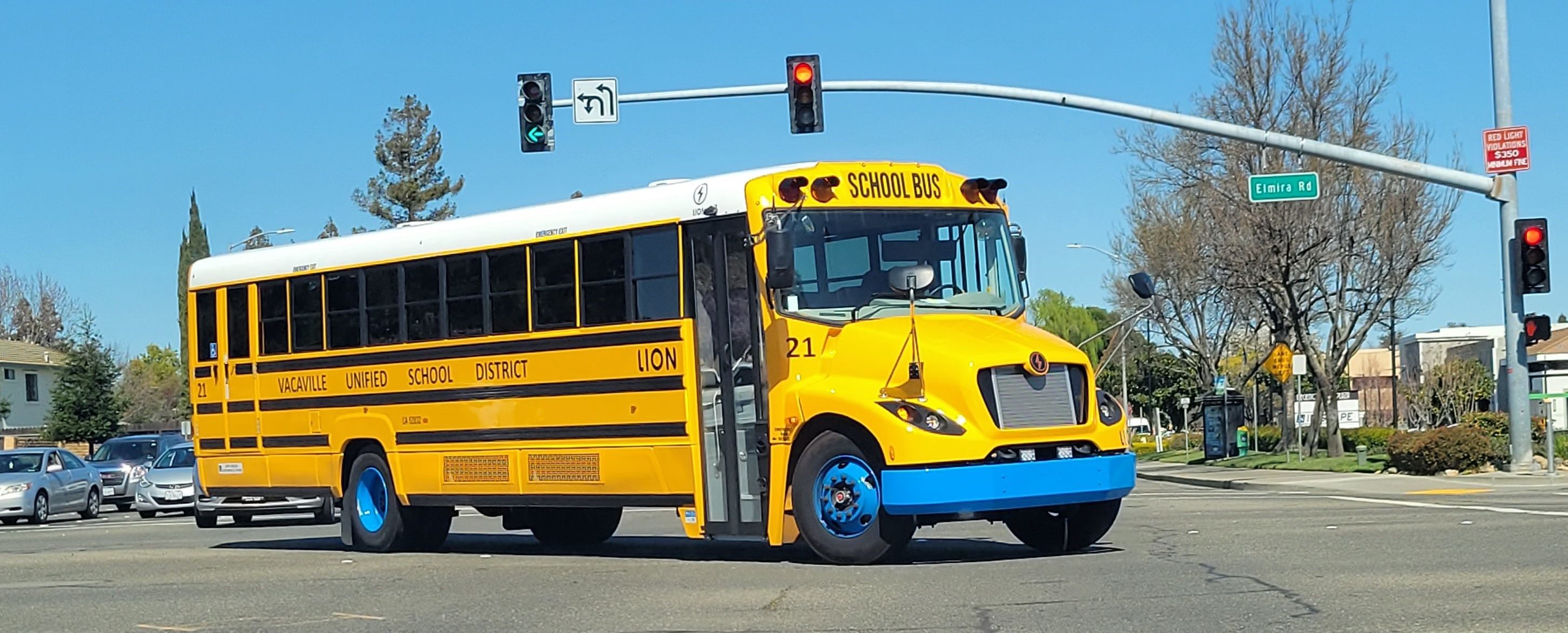 Yellow electric school bus driving through intersection.